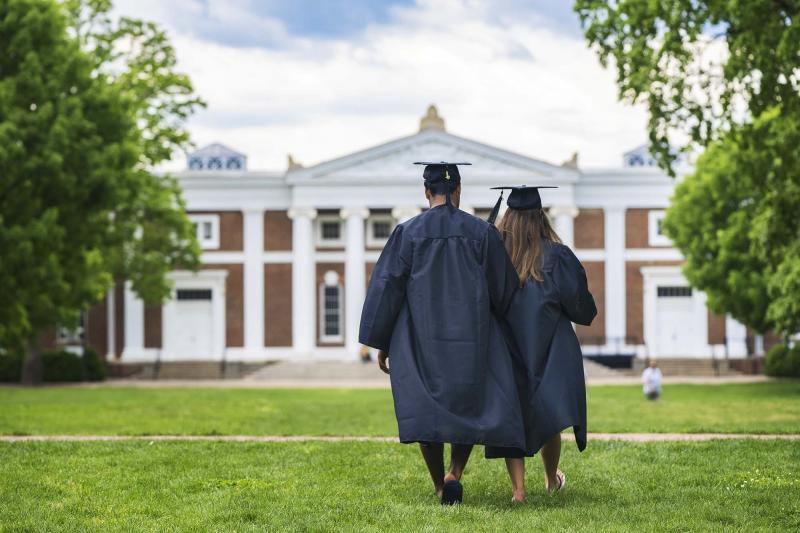 Two students in caps and gowns walking the lawn